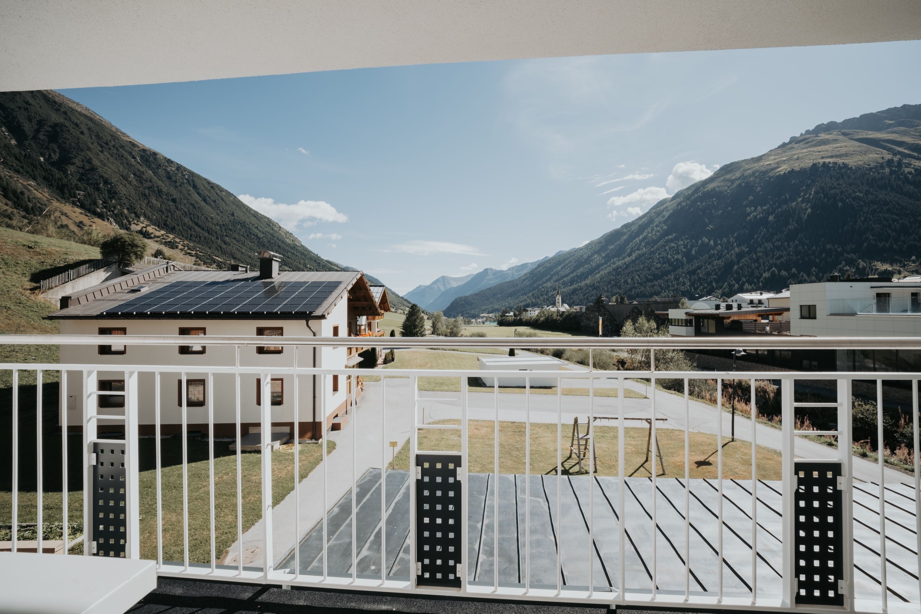 Blick von einem Balkon des Hauses über Wiesen und Nachbarhäuser bis zum Kirchturm von Galtür.
